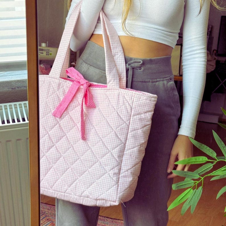 May include: A pink quilted tote bag with a white gingham pattern and a pink bow. The bag has a large capacity and is perfect for carrying everyday essentials.