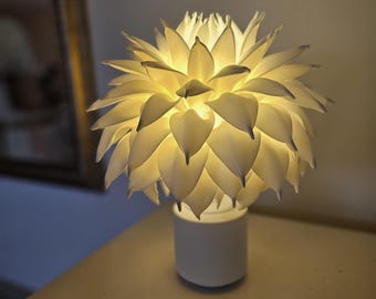 May include: A white table lamp shaped like a flower with a white base. The lamp is turned on and the light shines through the petals.