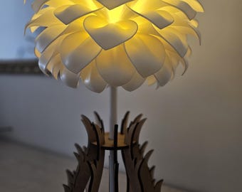 May include: A white flower-shaped lamp with a wooden base. The lamp is lit and the light shines through the white petals.