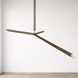 May include: A contemporary bronze ceiling light. The fixture has a central vertical rod and three horizontal rods extending outwards, each with a small, spherical light at the end. The light is suspended from the ceiling. The overall design is minimalist.