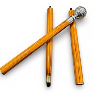 Könnte beinhalten: Ein hölzerner Gehstock mit einem silberfarbenen Kugelgriff und einem goldfarbenen Metallband am Fuß. Der Stock hat ein hellbraunes, gestreiftes Muster und ist vor einem weißen Hintergrund abgewinkelt.