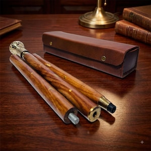Può includere: Un bastone da passeggio pieghevole in legno marrone lucido con dettagli in ottone e un'impugnatura metallica, accompagnato da una custodia rettangolare in pelle marrone con due bottoni a pressione in ottone, presentato in tre segmenti smontati.