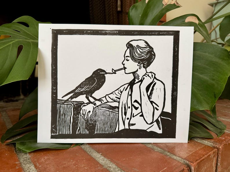 May include: Black and white linocut print featuring a woman with a bird. The woman is holding a lit cigarette, with the bird perched on a stack of books. The print has a vintage aesthetic.