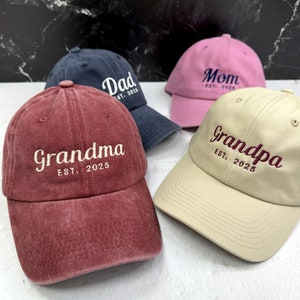 May include: Four baseball caps with different colors and embroidered text. The caps are labeled "Dad est. 2025", "Mom est. 2025", "Grandma est. 2025", and "Grandpa est. 2025".