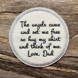 May include: A round, white patch with a silver stitched border. Black script reads: "The angels came and set me free so hug my shirt and think of me. Love, Dad."