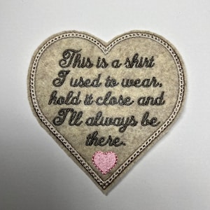 May include: A heart-shaped patch with embroidered text reading "This is a shirt I used to wear, hold it close and I'll always be there." The patch is beige with a pink heart and a decorative border.
