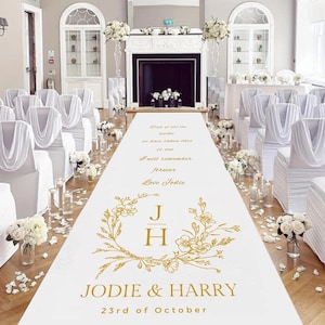 May include: A white wedding aisle runner with gold floral design and text. The runner features the names "Jodie & Harry" and the date "23rd of October". The aisle is decorated with flowers and candles, creating an elegant setting.