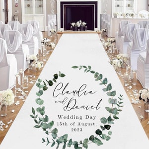 May include: White wedding aisle runner with a green eucalyptus wreath design. The wreath has the names "Claudia and Daniel" and the text "Wedding Day 15th of August, 2023".