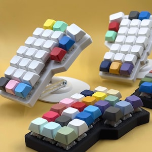 May include: Three different keyboard keycap sets with various colors, including pink, blue, green, yellow, orange, red, purple, gray, and brown. The keycaps are arranged in a grid pattern on a black and white base.