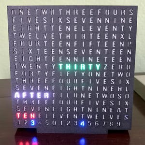 May include: A black, square word clock displaying the time. The clock face is made up of words that light up to indicate the time. The current time displayed is "Thirty After Ten". The numbers 1-9 are displayed at the bottom.