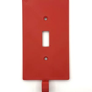 May include: A red plastic light switch cover with a hook on the bottom.
