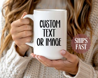 May include: White ceramic mug with the text "CUSTOM TEXT OR IMAGE" in black. The mug has a large handle and is held by a person. A brown sticker with the words "SHIPS FAST" is visible.