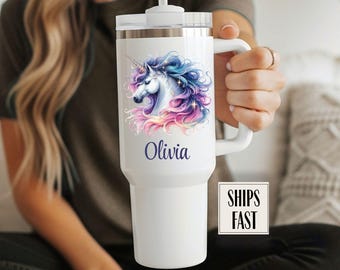 Könnte beinhalten: Weißer isolierter Becher mit einem bunten Einhorn-Design. Der Name "Olivia" ist darunter aufgedruckt. Der Becher hat einen Griff und einen Deckel mit Strohhalm.