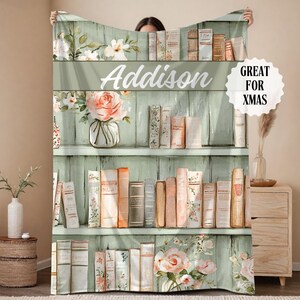 May include: A personalized blanket featuring a bookshelf design with the name "Addison" in white script. The blanket showcases a watercolor style with floral and book illustrations, and the text "GREAT FOR XMAS".