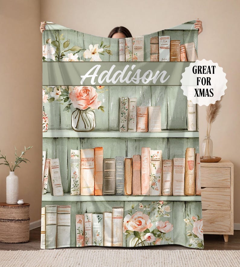 May include: A personalized blanket featuring a bookshelf design with the name "Addison" in white script. The blanket showcases a watercolor style with floral and book illustrations, and the text "GREAT FOR XMAS".