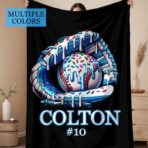May include: Black blanket with a baseball-themed design. It shows a baseball glove catching a baseball, both with a blue and white colour scheme and a dripping frosting effect with colourful sprinkles. The name "COLTON" and the number "#10" are displayed.