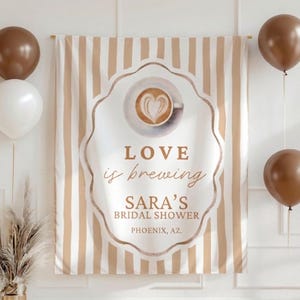 May include: A striped banner in beige and white, with a coffee cup design and the words "LOVE is brewing" and "SARA'S BRIDAL SHOWER, PHOENIX, AZ." The image includes brown and white balloons and a vase of dried plants, suitable for a bridal shower.