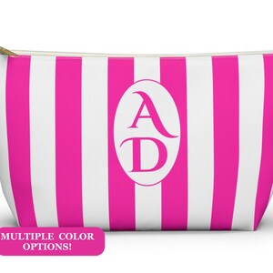 May include: A zipped pouch featuring vertical hot pink and white stripes with a central white oval containing the letters AD in a serif font. A pink rectangular label at the bottom left displays the text MULTIPLE COLOR OPTIONS!