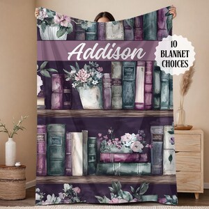 May include: A personalized blanket featuring a watercolor design of a bookshelf filled with books and floral arrangements. The name "Addison" is displayed prominently. The blanket has a purple and white color scheme, with the text "10 BLANKET CHOICES".