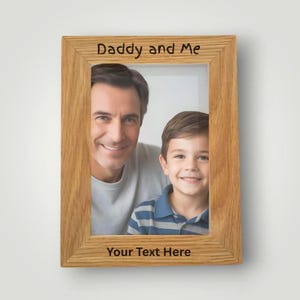 May include: A wooden picture frame with the text "Daddy and Me" at the top and "Your Text Here" at the bottom. The frame contains a photo of a man and a young boy.
