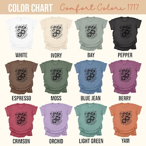 May include: A color chart of Comfort Colors 1717 t-shirts. Each shirt displays a black floral design. Colors include white, ivory, bay, pepper, espresso, moss, blue jean, berry, crimson, orchid, light green, and yam.