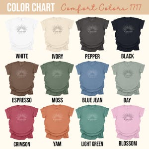 Op de afbeelding: Een kleurenkaart toont verschillende Comfort Colors t-shirts. De shirts zijn in verschillende kleuren, waaronder wit, ivoor, peper, zwart, espresso, mos, spijkerbroekblauw, baai, karmozijn, yam, lichtgroen en bloesem. Elk shirt heeft een zon-afbeelding en tekst.