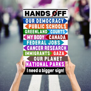 May include: A white sign with the text "HANDS OFF" in black letters. The sign has a list of items with arrows pointing to the left, including "OUR DEMOCRACY", "PUBLIC SCHOOLS", "GREENLAND", "COURTS", "MY BODY", "CANADA", "FEDERAL JOBS", "CANCER RESEARCH", "IMMIGRANTS", "GAZA", "OUR PLANET", and "NATIONAL PARKS". The sign also has the text "I need a bigger sign!" in black letters.