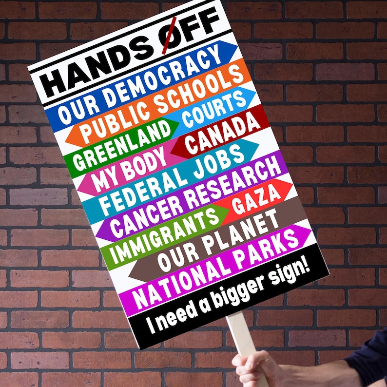 May include: A white sign with black text that reads "Hands Off" with a red line through the word "Off". The sign lists a variety of topics including "Our Democracy", "Public Schools", "Greenland Courts", "My Body", "Federal Jobs", "Cancer Research", "Immigrants", "Our Planet", and "National Parks". The sign also includes the text "I need a bigger sign!"