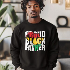 May include: Black sweatshirt with the text "PROUD BLACK FATHER" in white, red, yellow, and green. The sweatshirt is a crew neck style and appears to be made of a soft material. The design is centered on the chest.
