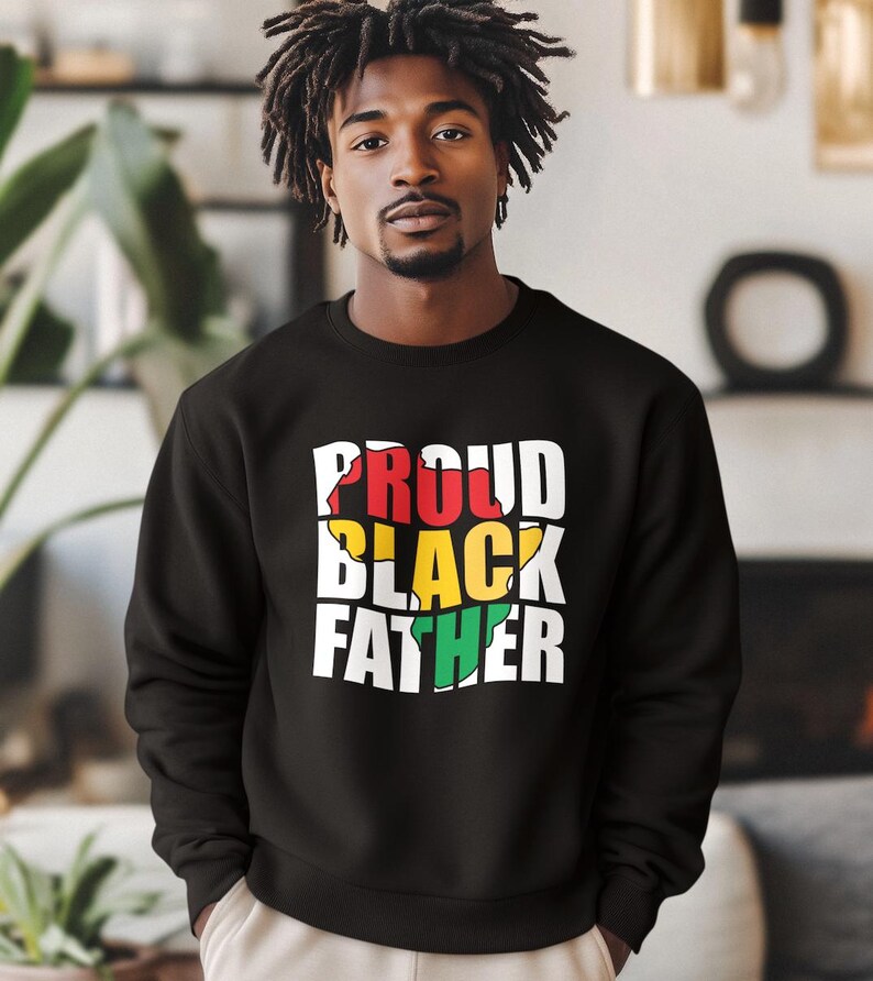 May include: Black sweatshirt with the text "PROUD BLACK FATHER" in white, red, yellow, and green. The sweatshirt is a crew neck style and appears to be made of a soft material. The design is centered on the chest.