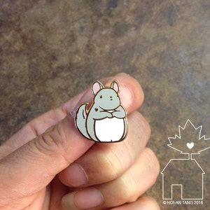 Mehoi Grey Chinchilla Hard Enamel Pin close up shown in hand with neutral brown backdrop