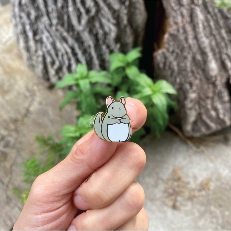 Mehoi Grey Chinchilla Hard Enamel Pin shown in hand with organic outdoor backdrop