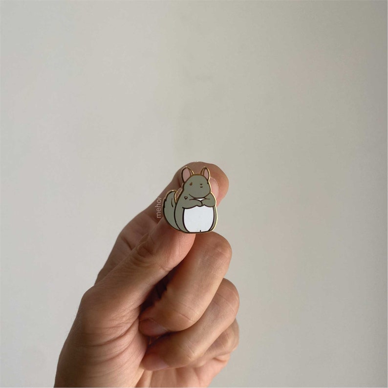 Mehoi Grey Chinchilla Hard Enamel Pin shown in hand with neutral backdrop