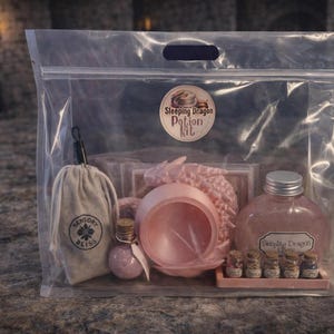 A clear plastic zipper bag containing a pink sleeping dragon potion kit with a cauldron, bottled elixir, and mini jars sitting on a stone surface.