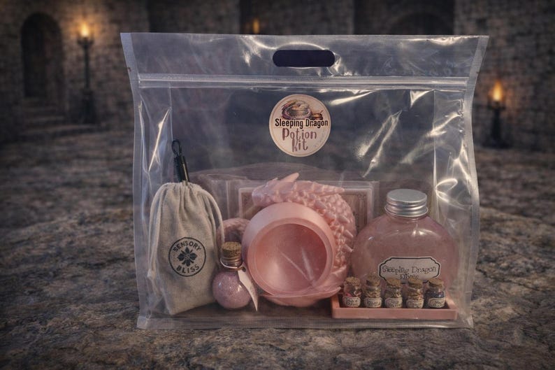 A clear plastic zipper bag containing a pink sleeping dragon potion kit with a cauldron, bottled elixir, and mini jars sitting on a stone surface.