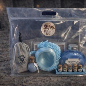 A clear plastic zipper bag containing a light blue sleeping dragon potion kit with a cauldron, bottled elixir, and mini jars sitting on a stone surface.