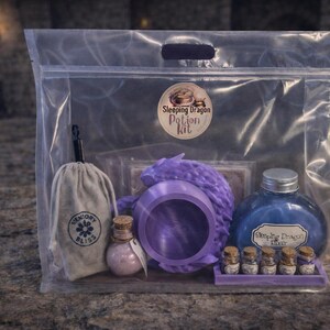 A clear plastic zipper bag containing a purple sleeping dragon potion kit with a cauldron, bottled elixir, and mini jars sitting on a stone surface.