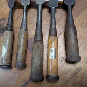 Puede incluir: Colecci&oacute;n de cinco formones de madera antiguos con hojas de metal. Los mangos son de madera envejecida, mostrando signos de desgaste. Los formones est&aacute;n dispuestos sobre una superficie de madera, mostrando su artesan&iacute;a.