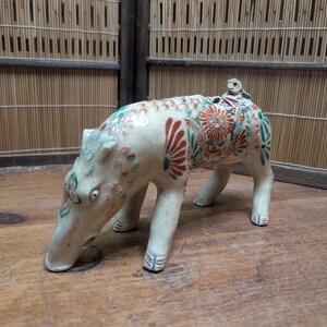 May include: A ceramic figurine of an animal with a long snout, possibly a tapir or similar creature. The figurine is cream-colored with red, green, and blue floral patterns. A small figure sits on its back.