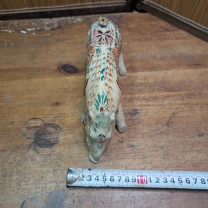 May include: A cream-colored, ceramic animal figurine with intricate floral and geometric patterns in red, green, and blue. The figurine is approximately 6 inches long, and is positioned on a wooden surface.