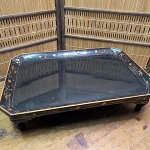 以下が含まれることがあります： 長方形の黒漆塗りサービングトレイ。装飾的な金色のアクセントが施されています。トレイは光沢のある仕上げで、短い濃い色の脚の上に置かれています。エッジには花柄と幾何学模様があります。