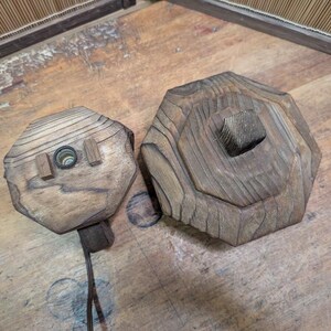 May include: Two wooden, hexagonal-shaped objects. One has a hole with a light fixture and two small wooden blocks. The other has a square hole in the center. Both are made of light brown wood with visible grain.