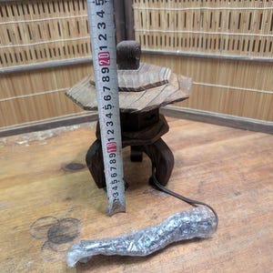 May include: A small, wooden Japanese garden lantern with a tiered roof and a dark brown finish. The lantern is approximately 5 inches tall and has a base with three legs. A measuring tape is placed next to the lantern.