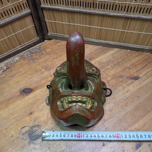 Op de afbeelding: Een vintage Japanse Tengu-masker, met een lange neus en een felle uitdrukking. Het masker is geschilderd in groen, rood en goud, met tekenen van slijtage. Het is een traditioneel item dat wordt gebruikt in de Japanse folklore en theater.