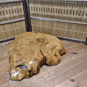 Puede incluir: Una mesa de losa de madera natural con una forma orgánica única. La mesa es de color marrón cálido con vetas de madera visibles y un acabado brillante. La mesa tiene aproximadamente 76 cm de diámetro y es adecuada para una variedad de usos.