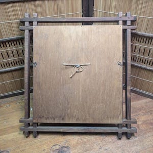 May include: A wooden framed square panel, likely the back of a mirror or artwork, with a natural wood grain finish. The frame is constructed of dark, rectangular wooden pieces joined at the corners. A natural fiber cord is tied to the center of the panel.