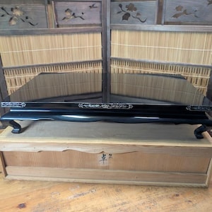 May include: A black lacquered display shelf with white decorative accents, on a wooden box. The shelf has curved legs and a reflective surface. The background features a wooden screen with bamboo and floral cutouts.