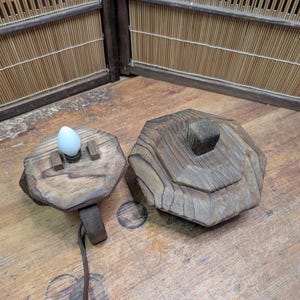 May include: A rustic wooden lamp with a unique, geometric design. The lamp features a light bulb and a separate wooden base. The wood has a natural, weathered appearance, adding to its charm. The lamp is designed to sit on a table or desk.