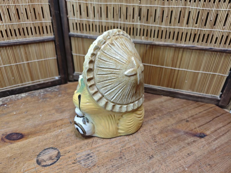 May include: A ceramic Tanuki figurine, a traditional Japanese raccoon dog, with a large hat and a sake bottle. The figurine is tan and cream-colored, with detailed carving and a whimsical design. The figurine is on a wooden surface.