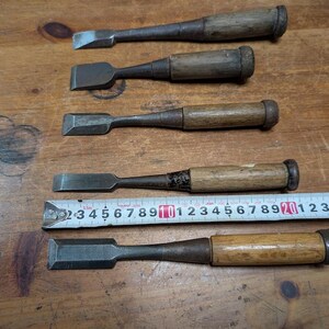 Puede incluir: Cinco cinceles de madera antiguos con hojas de metal, dispuestos sobre una superficie de madera. Una cinta m&eacute;trica se coloca junto a los cinceles. Los cinceles tienen mangos de madera y hojas de metal de varias formas y tama&ntilde;os.